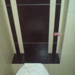 Ukończona aranżacja łazienki z brązowo-białymi pasami na suficie nad toaletą, widoczne fugi i fragment toalety z drobnymi zabrudzeniami.